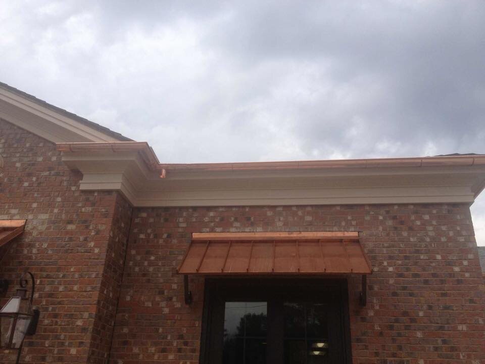 Copper gutter and a standing-seam copper awning on a red brick home