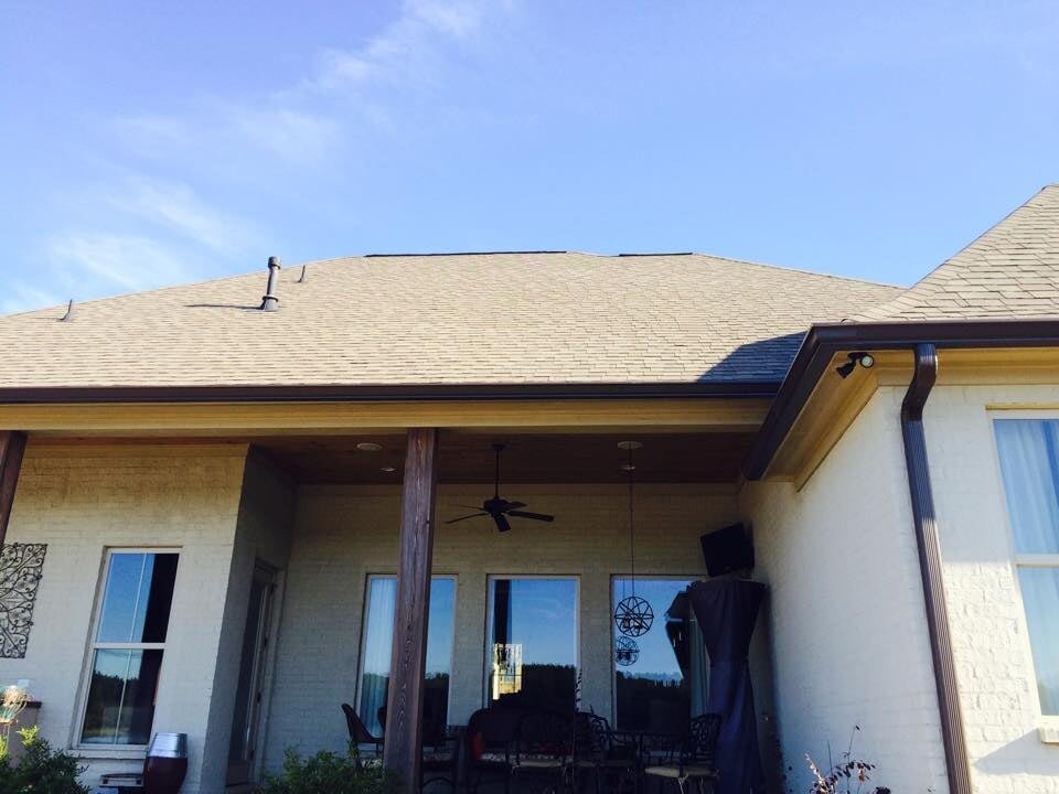 Rear covered patio on a light stucco home with a bronze gutter and downspout at the roof corner
