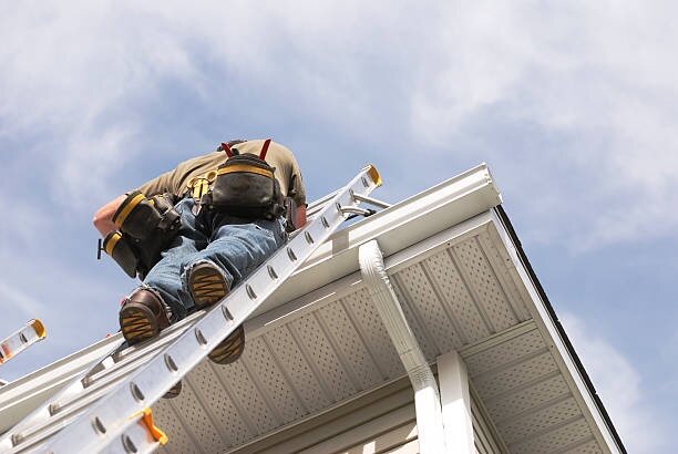 Installer on an extension ladder working at the eave of a house, seen from below