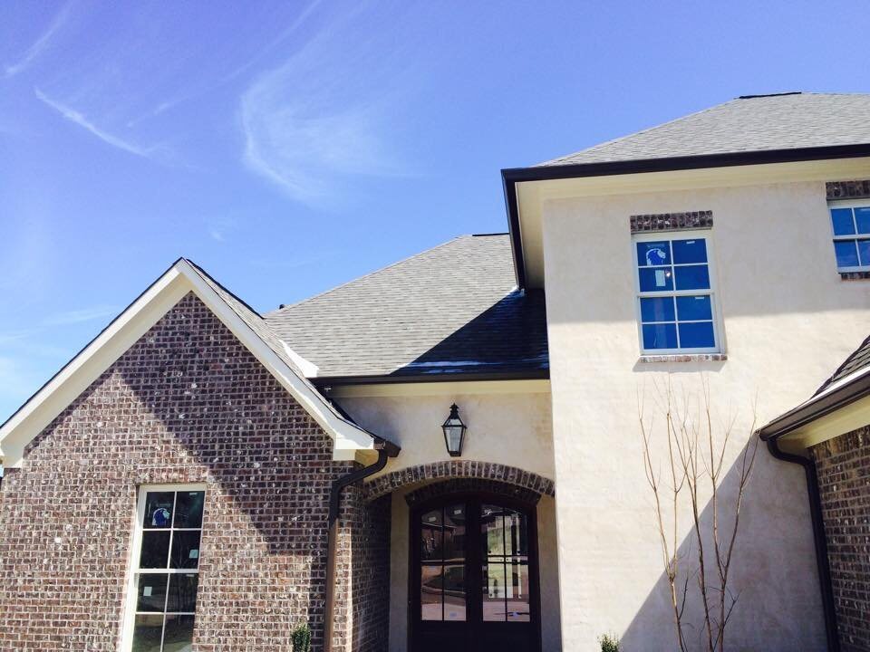 Brick and stucco two-story home with dark gutters and downspouts along the roofline
