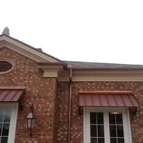 Copper standing-seam awnings over the windows of a brick home with a copper downspout